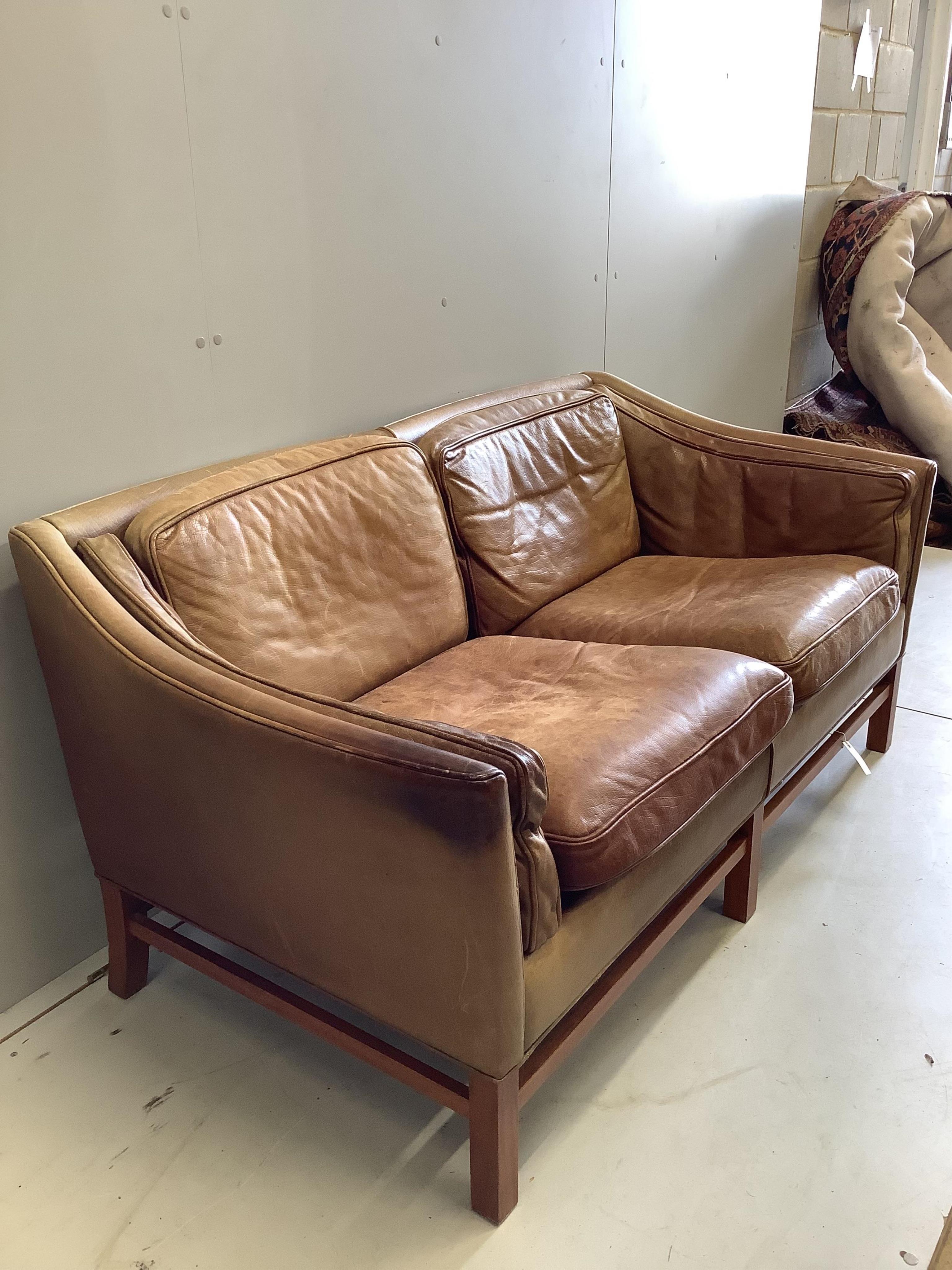 A mid century Danish teak and faded tan leather upholstered two seater settee, width 153cm. Condition - heavily faded from a light burgundy tone now down to pale tan